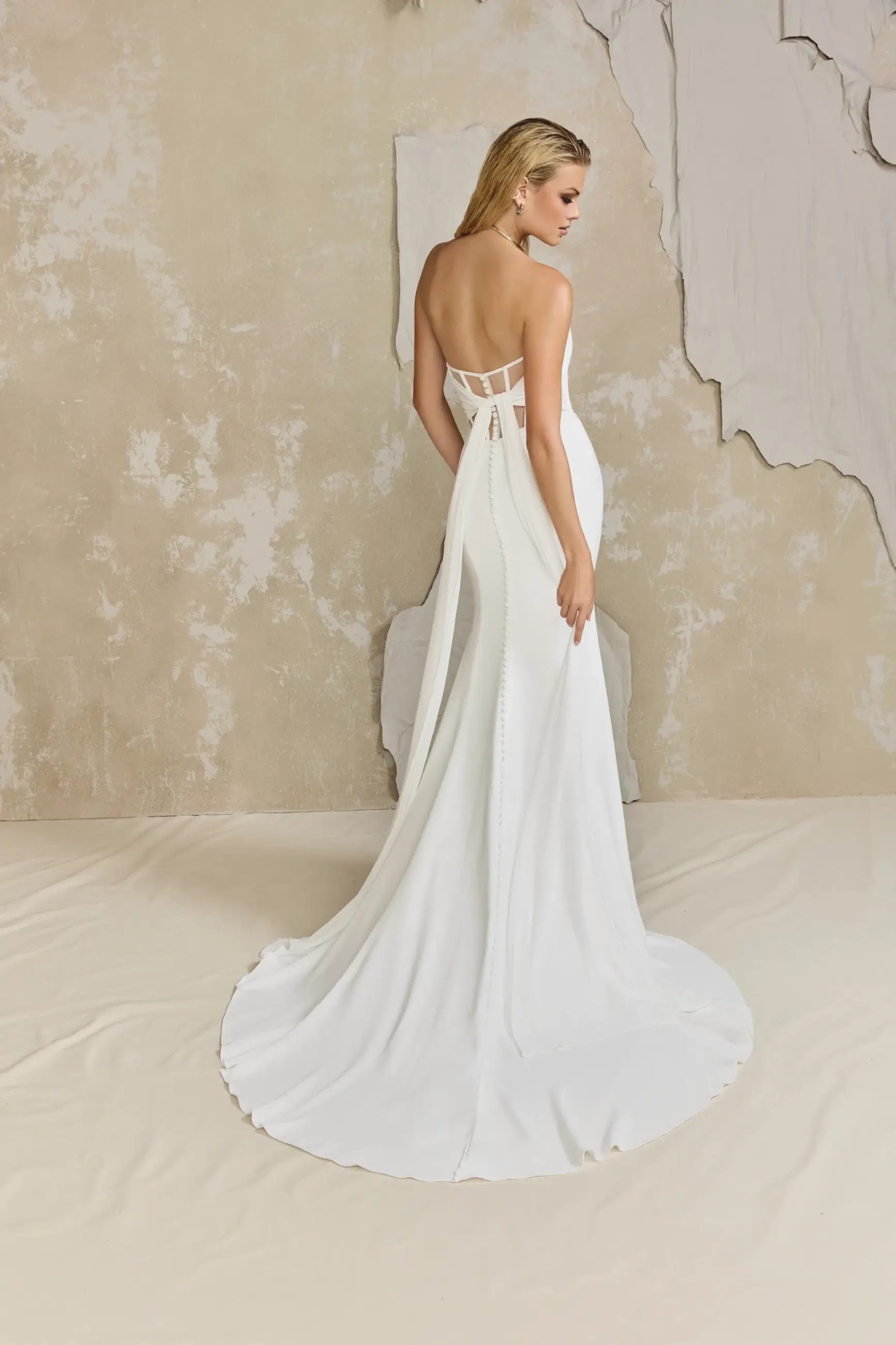 Model is wearing a chiffon and crepe fit and flare wedding dress with a chapel length train