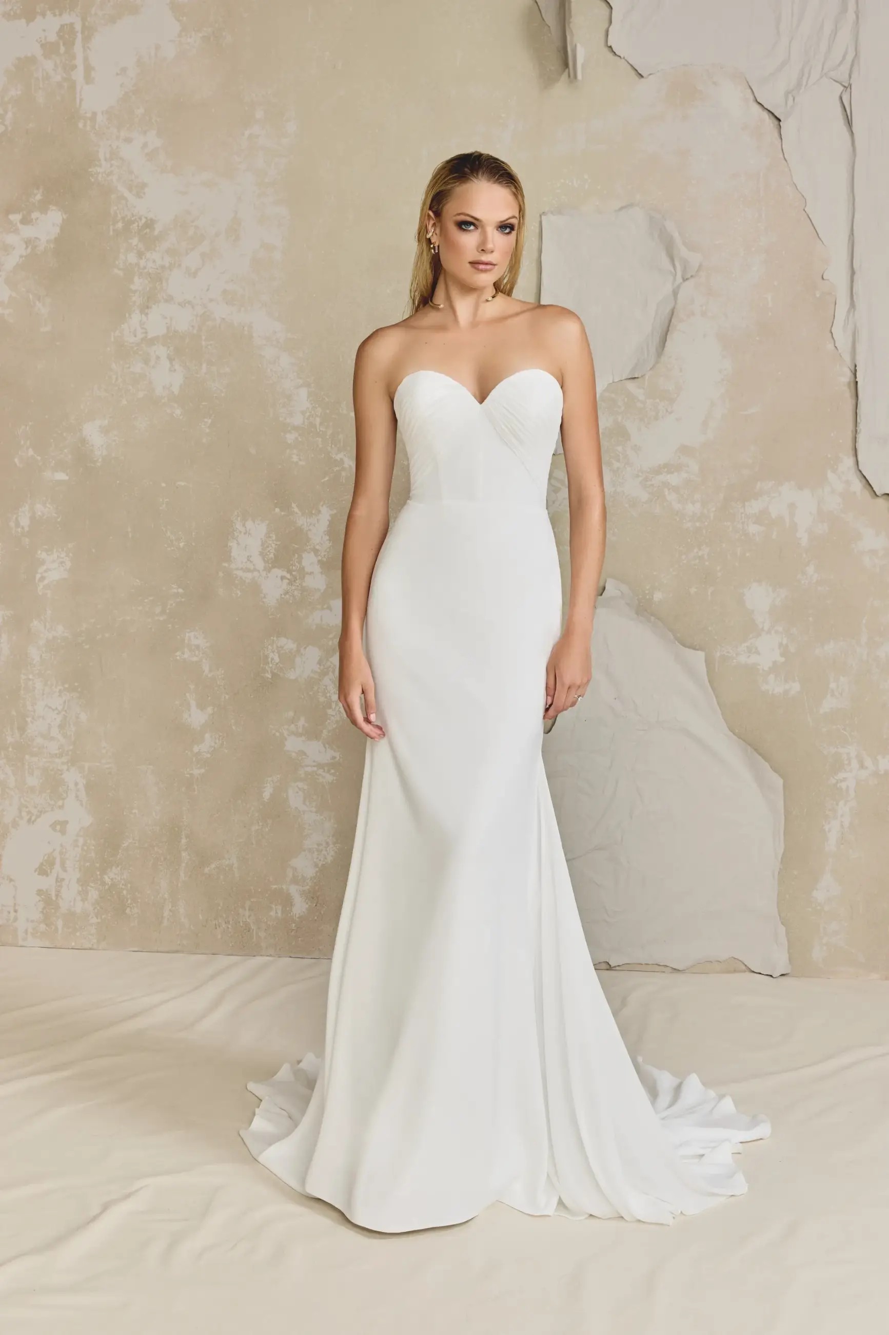 Model is wearing a chiffon and crepe fit and flare wedding dress with a chapel length train
