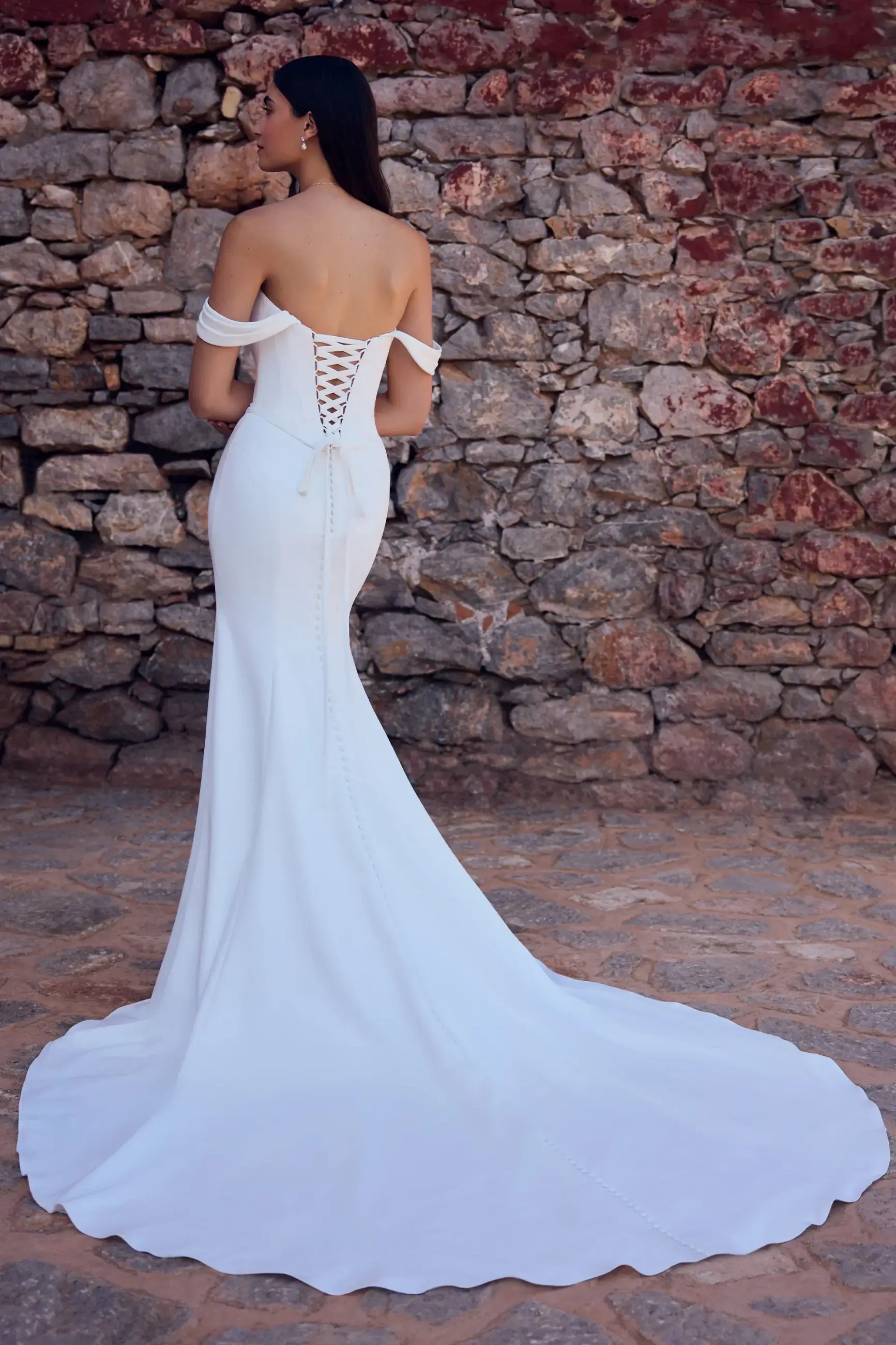 Model is wearing a matte satin sheath wedding dress with a corset lace up back