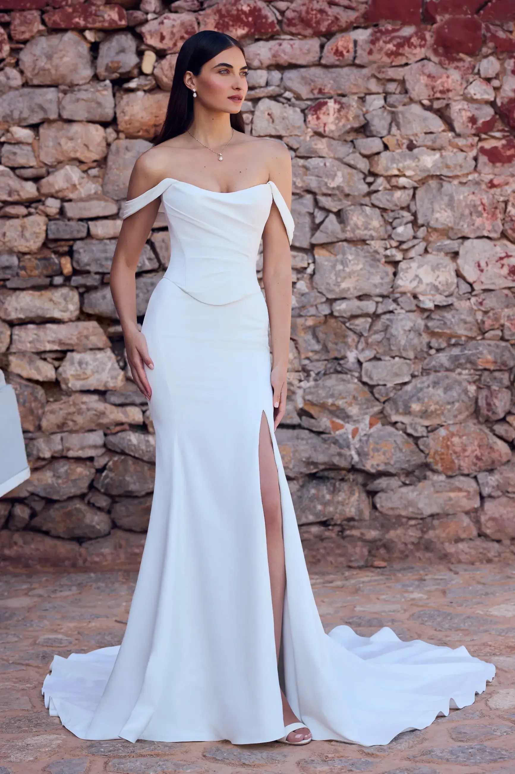 Model is wearing a matte satin sheath wedding dress with a corset lace up back